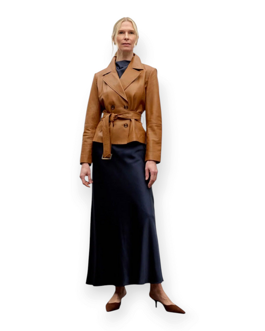 Birdie by Nina Liddle Design tan lambskin leather belted jacket with notched lapels worn over a navy satin skirt.