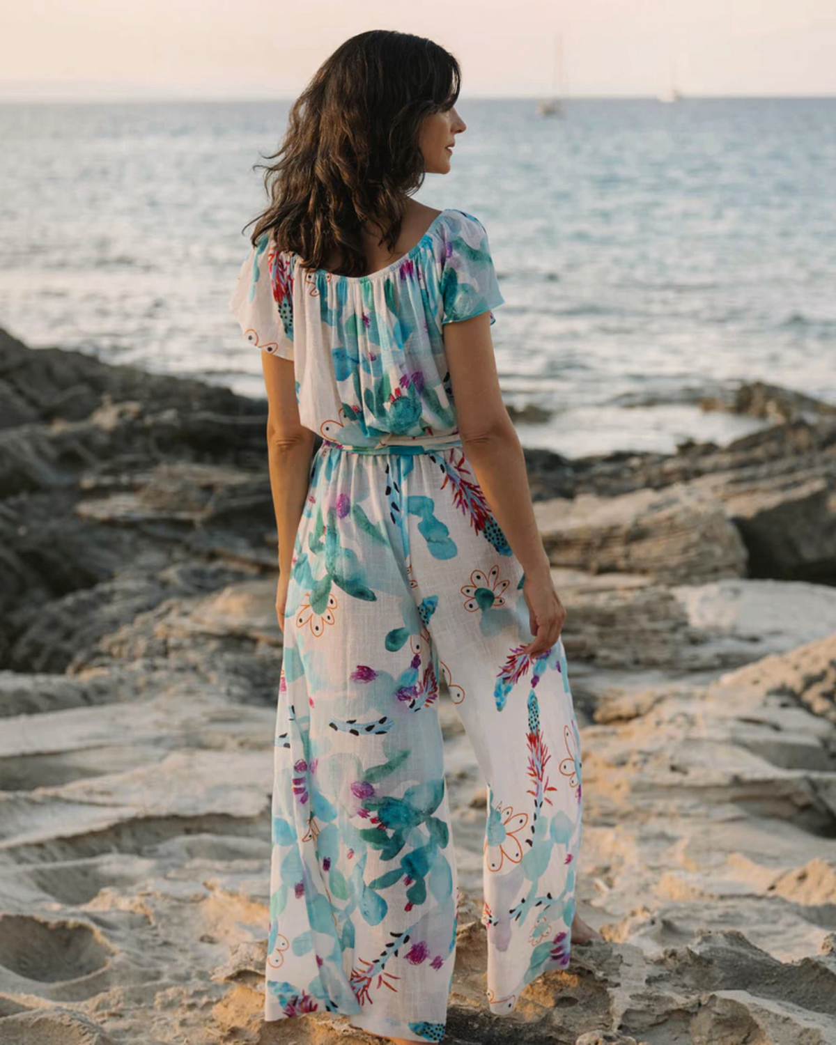 Birdie by Nina Liddle Design Dani jumpsuit in white cotton linen with blue and red floral print at a beach