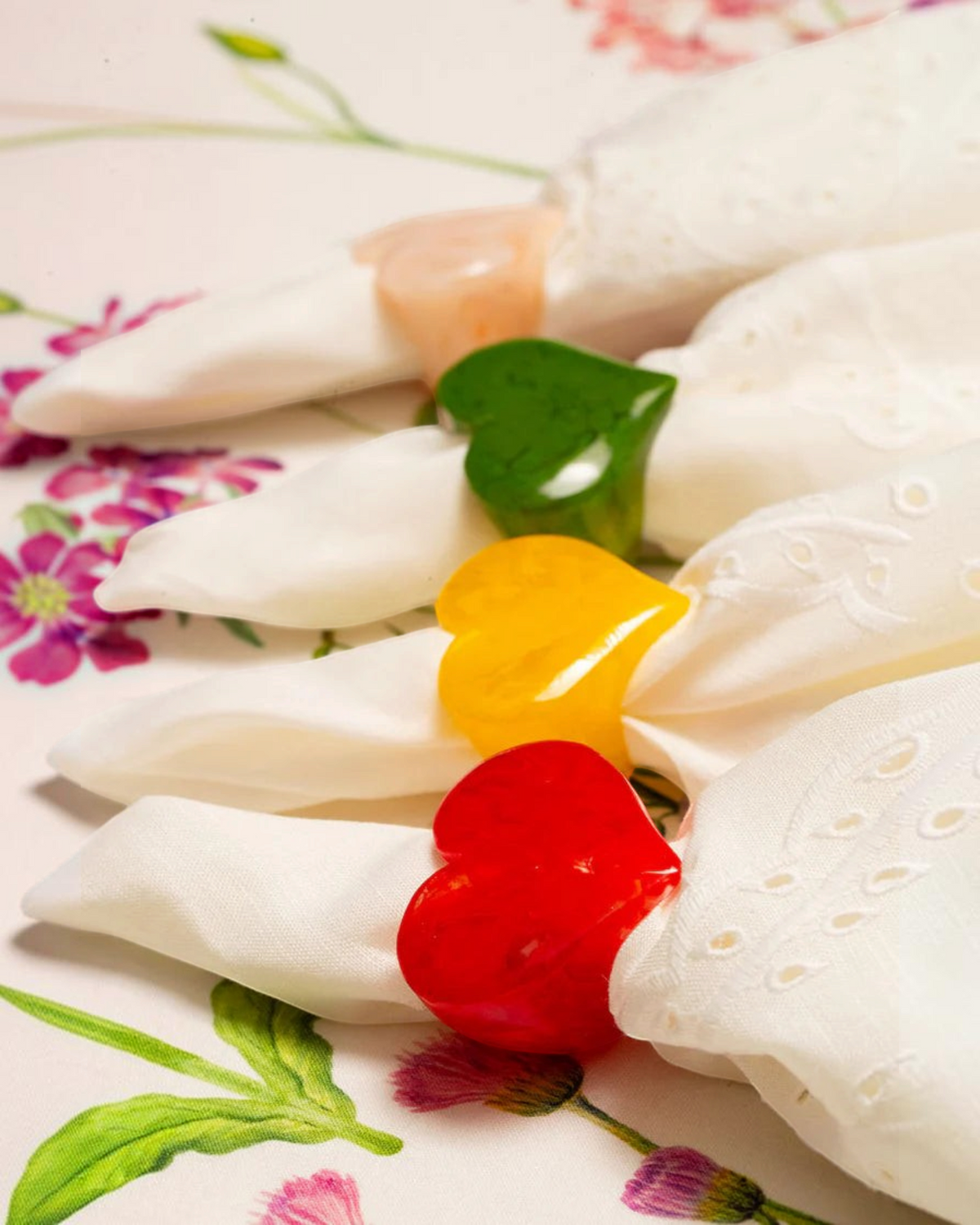 Birdie by Nina Liddle Design heart-shaped resin napkin rings in red, yellow, green, and peach on white napkins.